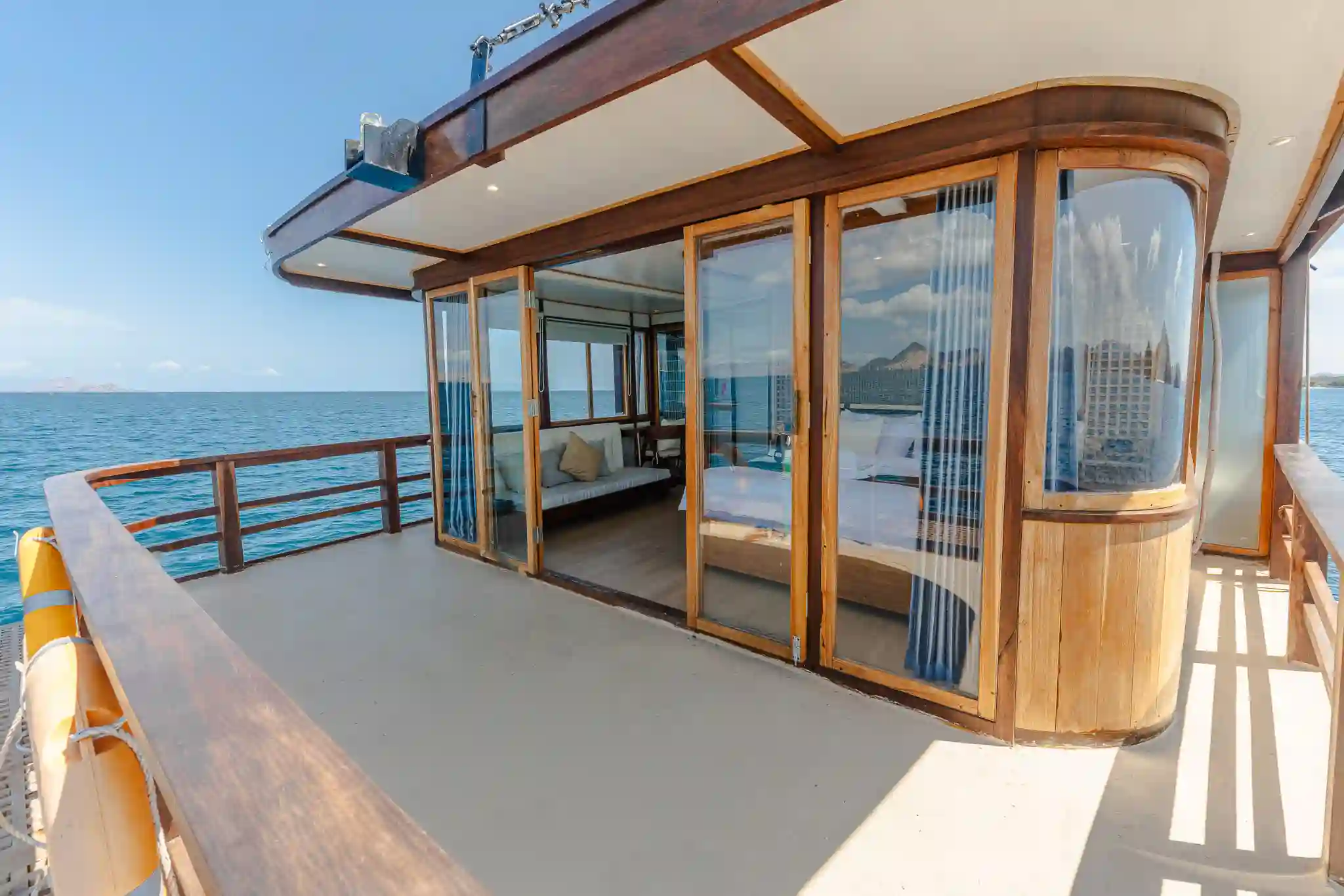 A luxury cabin interior featuring a king-sized bed, large windows with a direct sea view, and elegant wooden craftsmanship