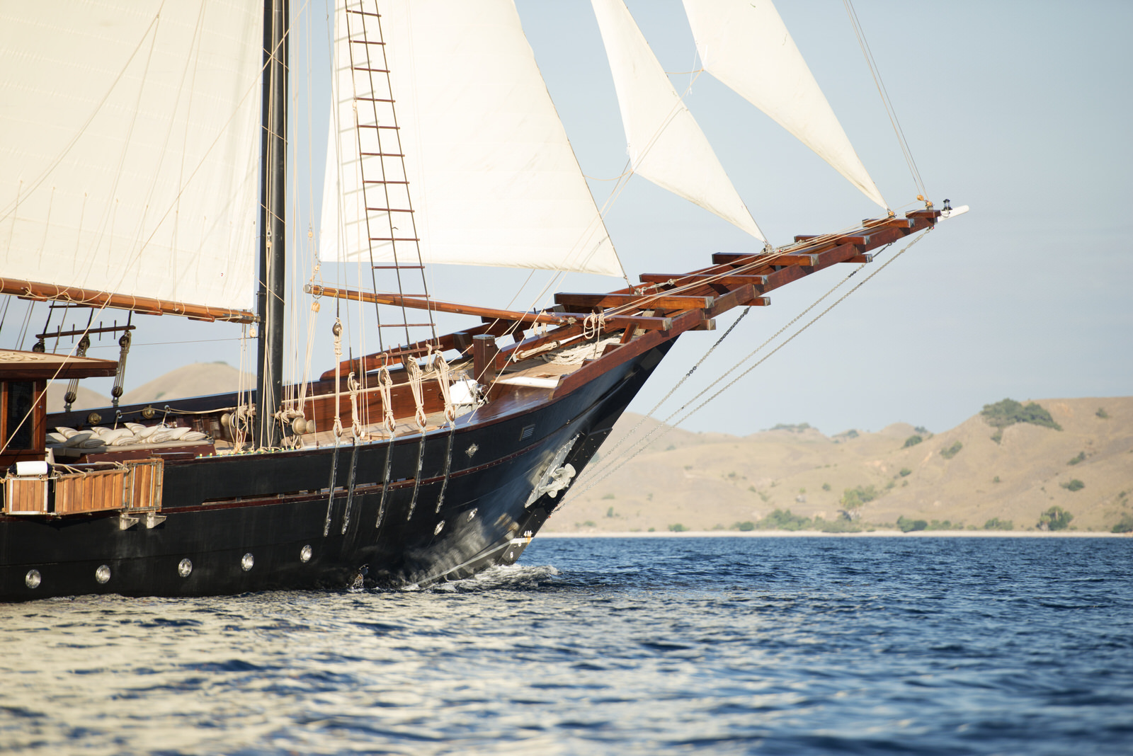 Traditional wooden phinisi yacht sailing across calm tropical waters, showcasing an authentic phinisi cruise Indonesia experience with elegant sails and scenic island landscapes.