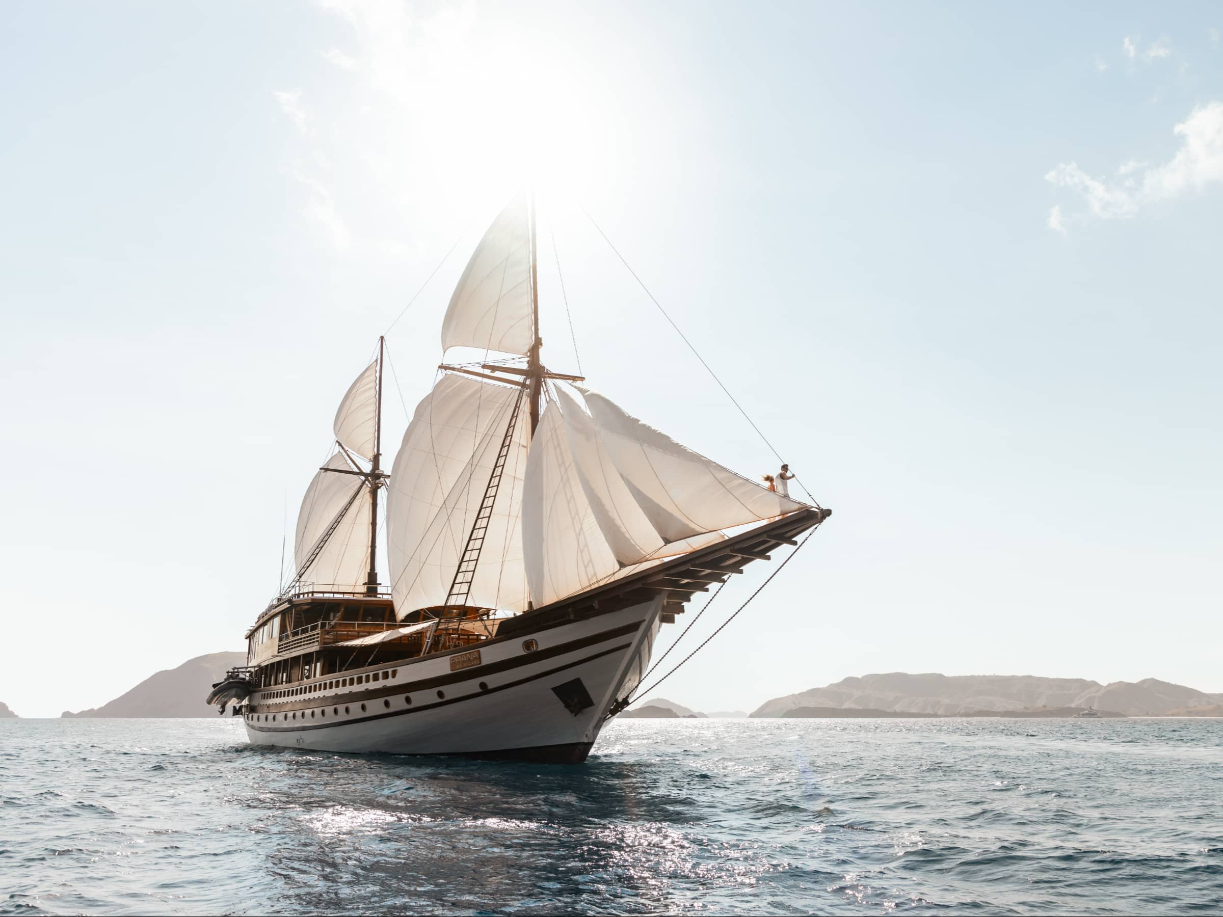 Luxury traditional sailing yacht cruising over clear blue waters, showcasing a classic phinisi cruise Indonesia experience with elegant white sails and a scenic tropical seascape